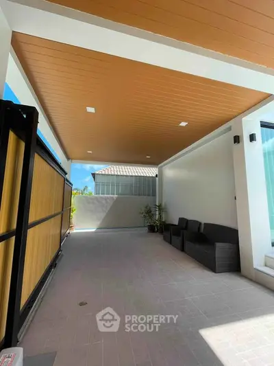 Spacious covered outdoor area with modern seating and wooden ceiling, perfect for relaxation.