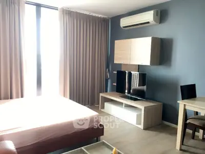 Modern bedroom with sleek furniture and natural light, featuring a mounted TV and air conditioning.