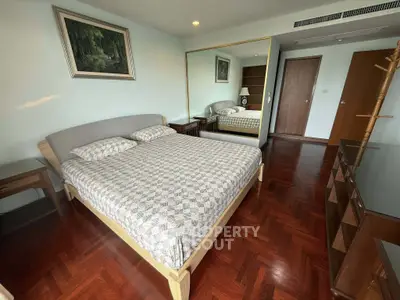 Spacious bedroom with elegant parquet flooring and large mirror reflecting natural light.