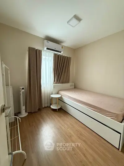 Cozy bedroom with natural light and minimalist decor, featuring a single bed and air conditioning.