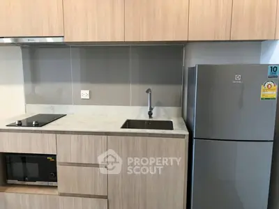 Modern kitchen with sleek cabinetry, built-in microwave, and stainless steel fridge in compact layout.