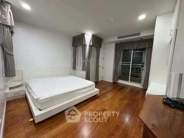 Spacious bedroom with wooden flooring and large windows in modern apartment.