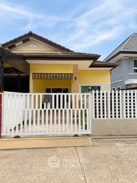 Charming single-story yellow house with gated entrance and tiled roof in a suburban neighborhood.