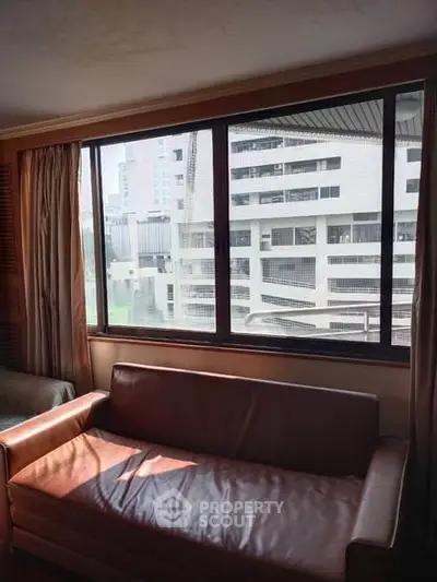 Spacious living room with large window offering urban view and natural light.