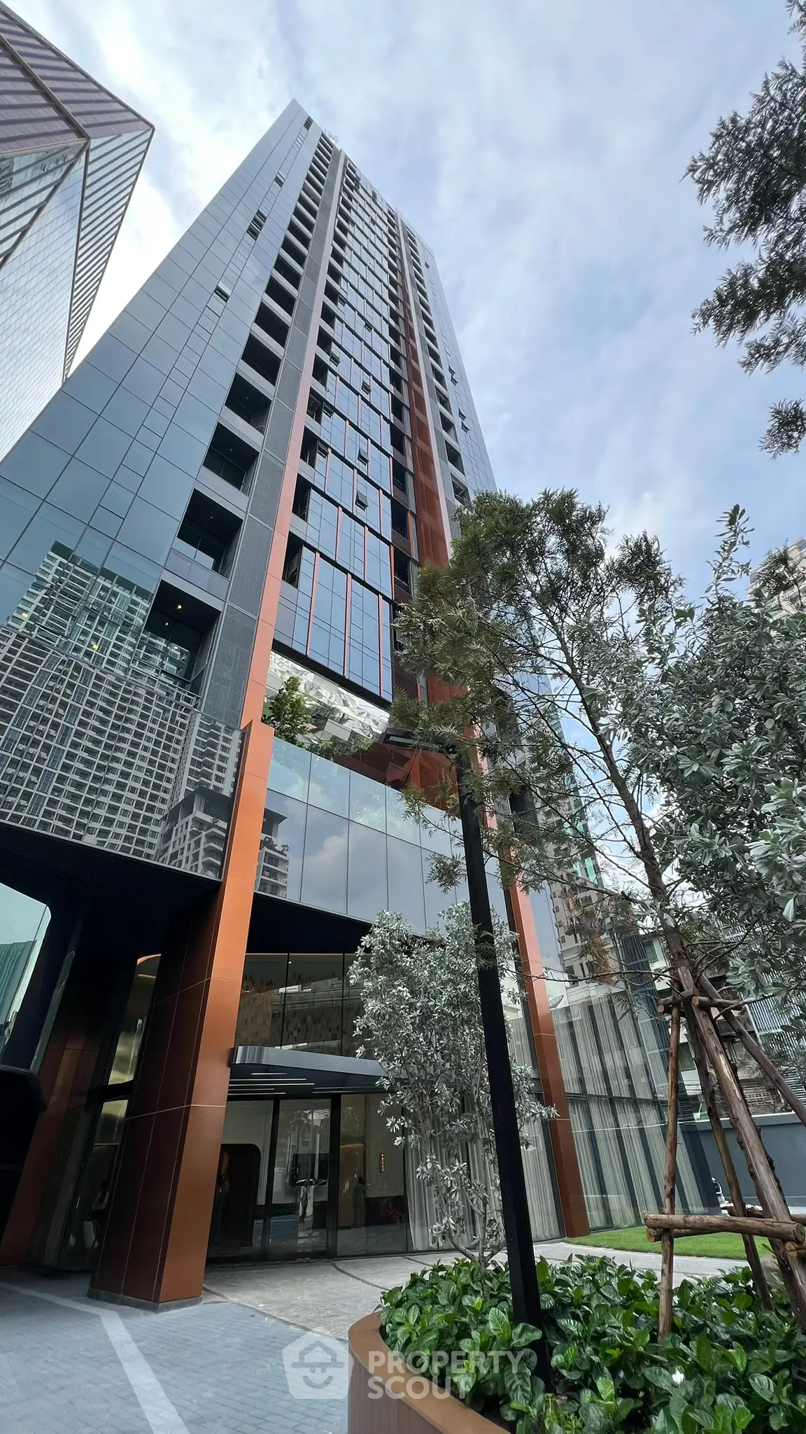 Stunning modern high-rise building with sleek glass facade and lush landscaping in urban setting.