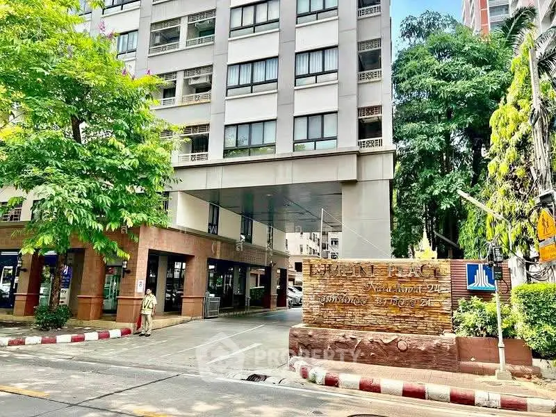 Modern apartment building entrance with lush greenery and clear signage in urban setting.