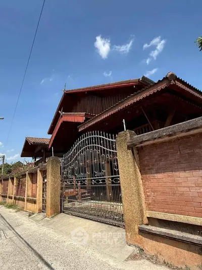 Charming traditional wooden house with ornate gate and brick fence under clear blue sky.