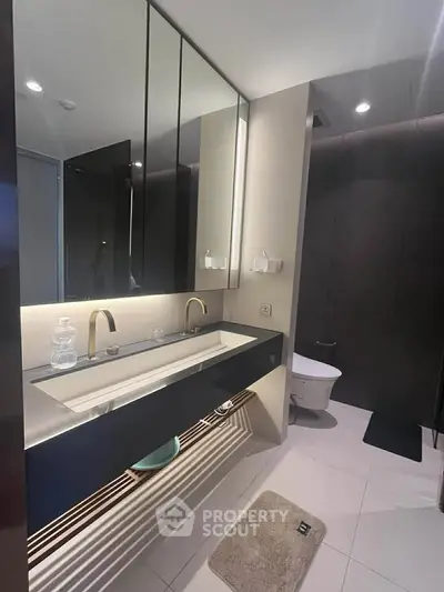 Modern bathroom with sleek design, featuring a large mirror, elegant sink, and contemporary fixtures.