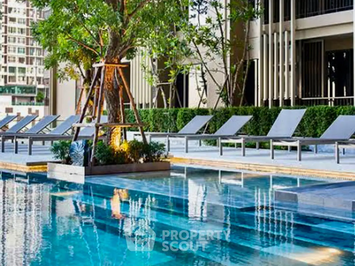 Luxurious apartment pool area with modern lounge chairs and lush greenery.