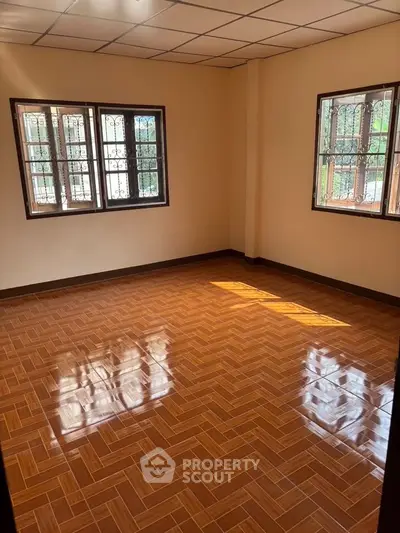 Spacious empty room with polished wooden flooring and large windows for natural light.