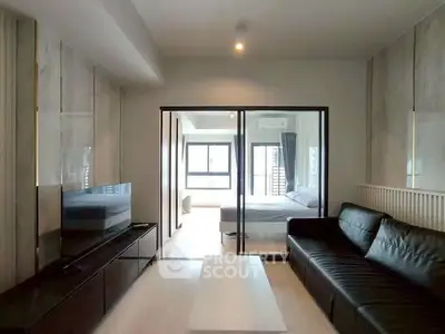 Modern living room with sleek black sofa and glass partition leading to a bright bedroom.