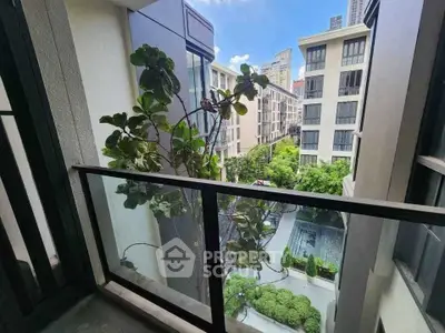 Modern urban balcony with glass railing overlooking lush courtyard and cityscape.