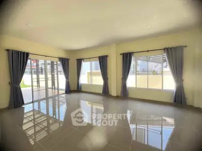 Spacious sunlit living room with large windows and elegant curtains.