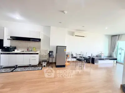 Spacious open-plan living room with modern kitchen and dining area, featuring sleek appliances and wooden flooring.