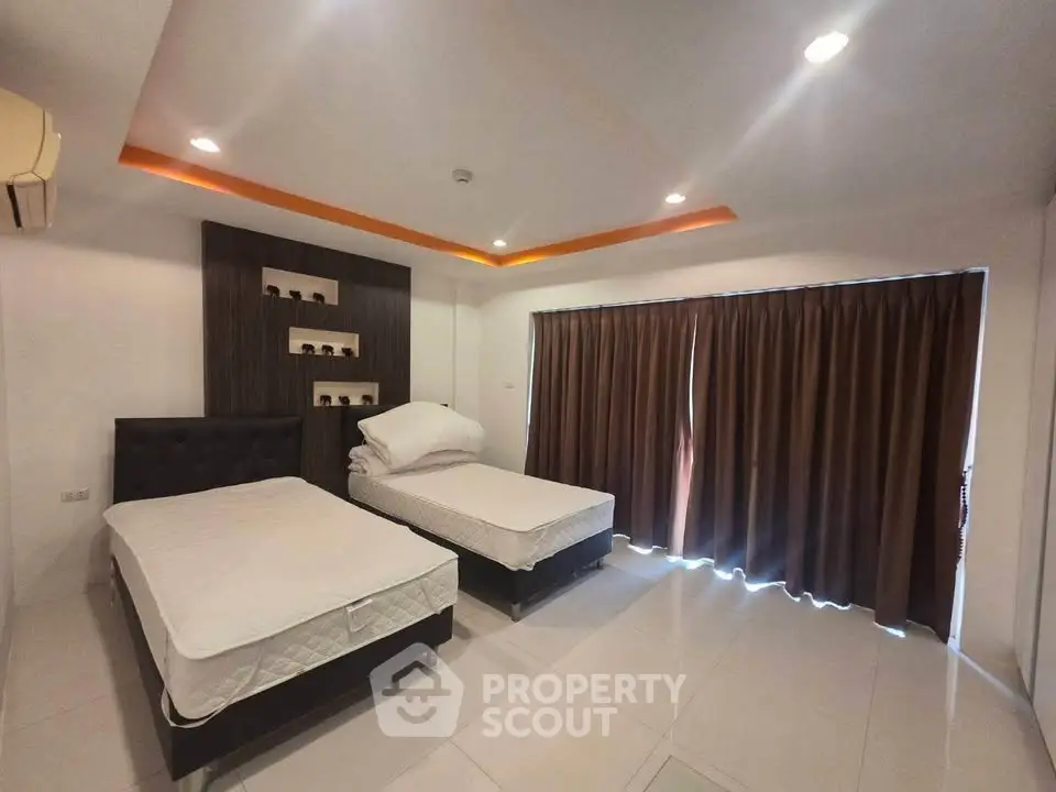 Spacious bedroom with two beds, modern lighting, and large window with curtains.