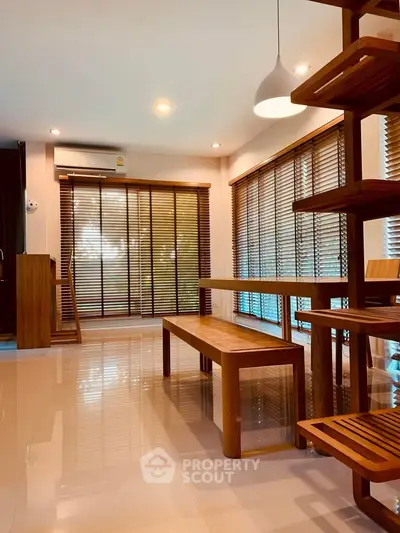 Modern living room with wooden furniture and large windows with blinds, creating a warm and inviting atmosphere.