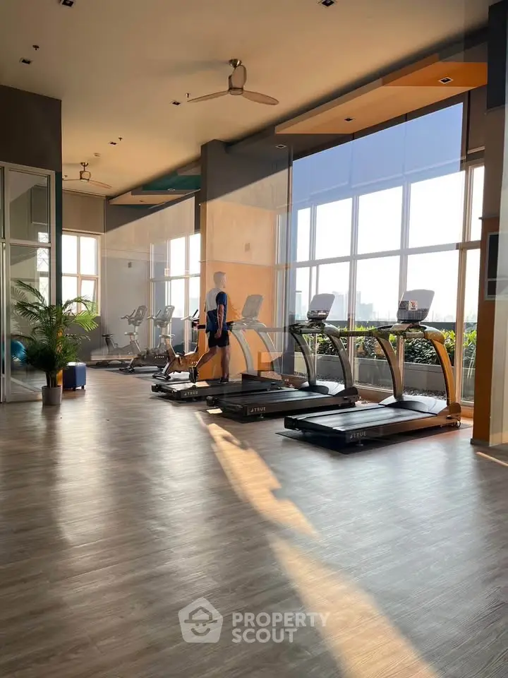 Spacious gym with modern equipment and large windows offering city views.