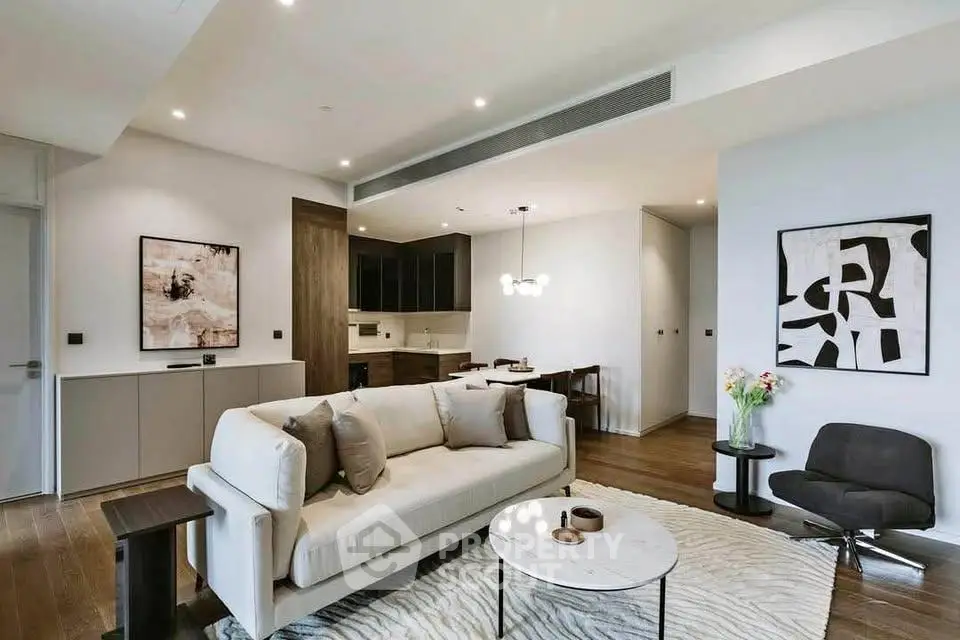 Modern living room with stylish decor and open kitchen layout, featuring elegant furniture and contemporary art.
