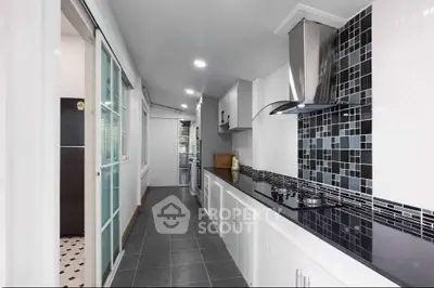 Modern kitchen with sleek black countertops and stylish backsplash in a narrow layout.
