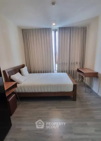 Modern bedroom with wooden furniture and large window, featuring elegant curtains and sleek flooring.