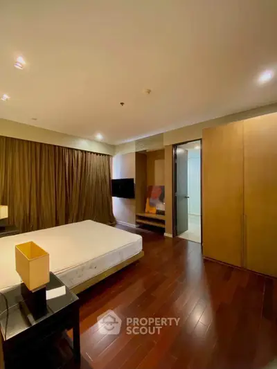 Spacious bedroom with wooden flooring and modern furnishings in a luxury apartment.