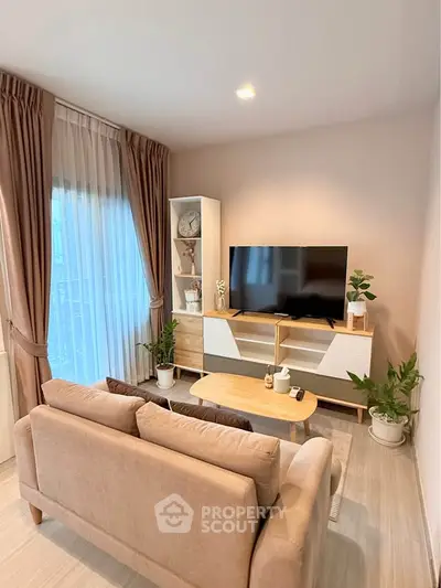 Modern living room with stylish furniture and large TV, featuring natural light and cozy ambiance.