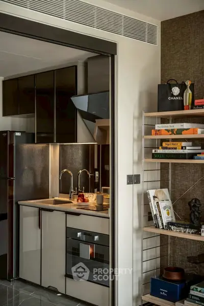 Modern kitchen with sleek cabinetry and built-in oven, adjacent to stylish shelving with books and decor.