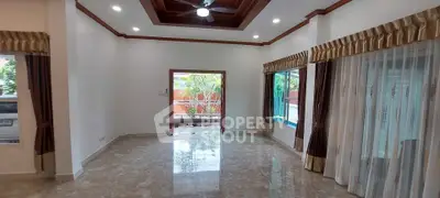 Spacious living room with large windows and elegant curtains, featuring a ceiling fan and polished floors.