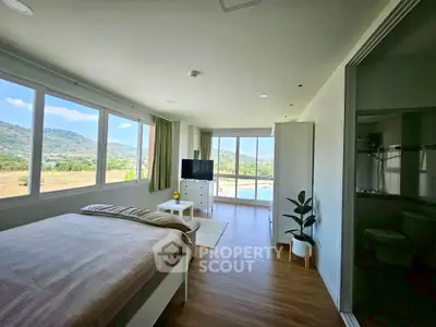 Spacious bedroom with panoramic windows offering stunning mountain and water views, featuring modern decor and natural light.