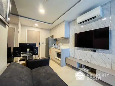 Modern living room with sleek kitchen and large TV, featuring stylish decor and air conditioning.