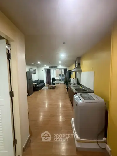 Spacious open-layout living room with modern kitchen and washing machine, perfect for urban living.