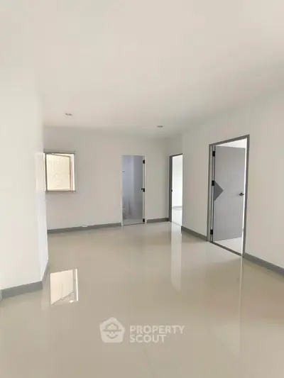 Spacious empty room with glossy tiled floors and multiple doorways, ideal for customization.