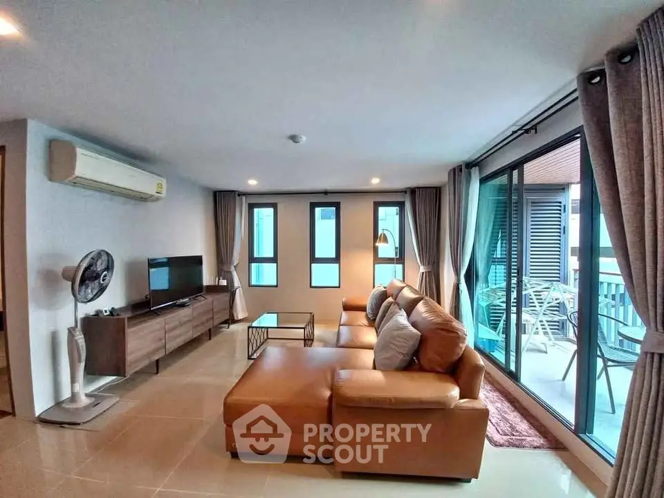 Spacious living room with modern furniture and large windows leading to a balcony.