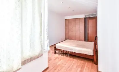 Spacious bedroom with wooden flooring and ample natural light in modern apartment.