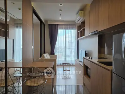 Modern open-layout living room with kitchen, featuring sleek wooden cabinetry and large windows for natural light.