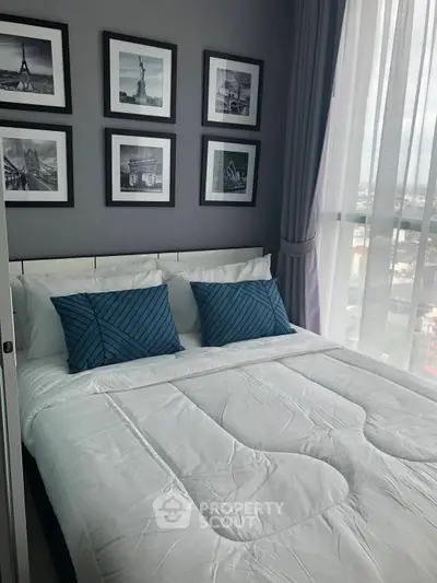Modern bedroom with stylish decor and city view, featuring elegant framed artwork and plush bedding.