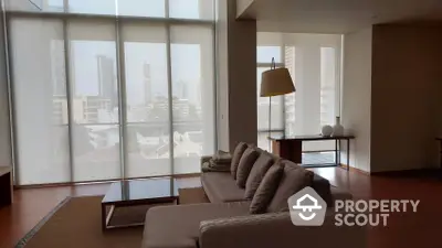 Expansive living room with floor-to-ceiling windows offering a panoramic city view, complemented by sleek modern furniture and warm wooden flooring.