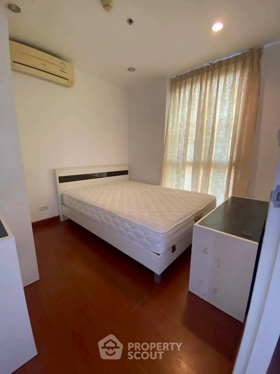 Cozy bedroom with wooden flooring and natural light, featuring a comfortable bed and air conditioning.