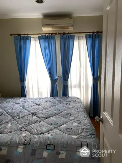 Cozy bedroom with natural light filtering through blue curtains, complete with air conditioning for comfort.