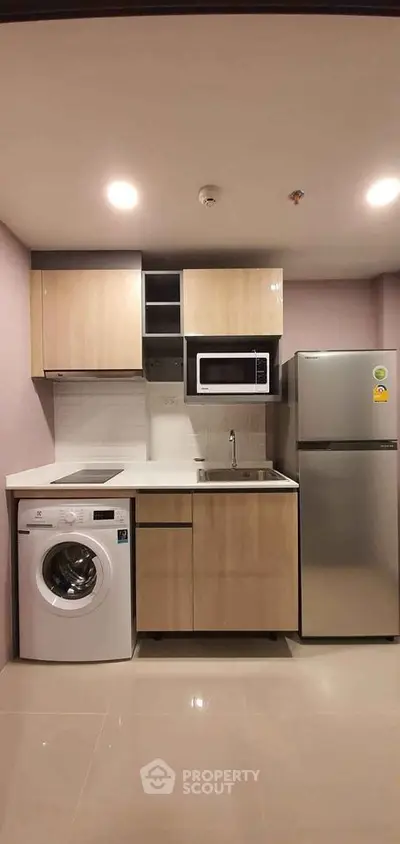 Modern compact kitchen with washing machine, microwave, and fridge in sleek apartment.