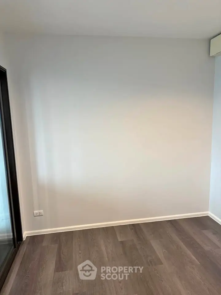 Spacious empty room with wooden flooring and large window, perfect for customization.