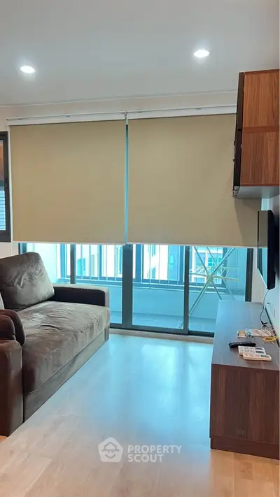 Modern living room with cozy sofa and large windows leading to a balcony, featuring sleek wooden furniture.