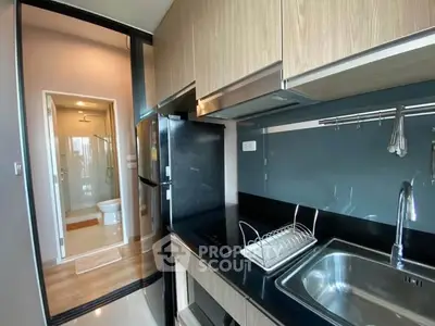 Modern kitchen with sleek cabinetry and view into bathroom, featuring stainless steel sink and appliances.