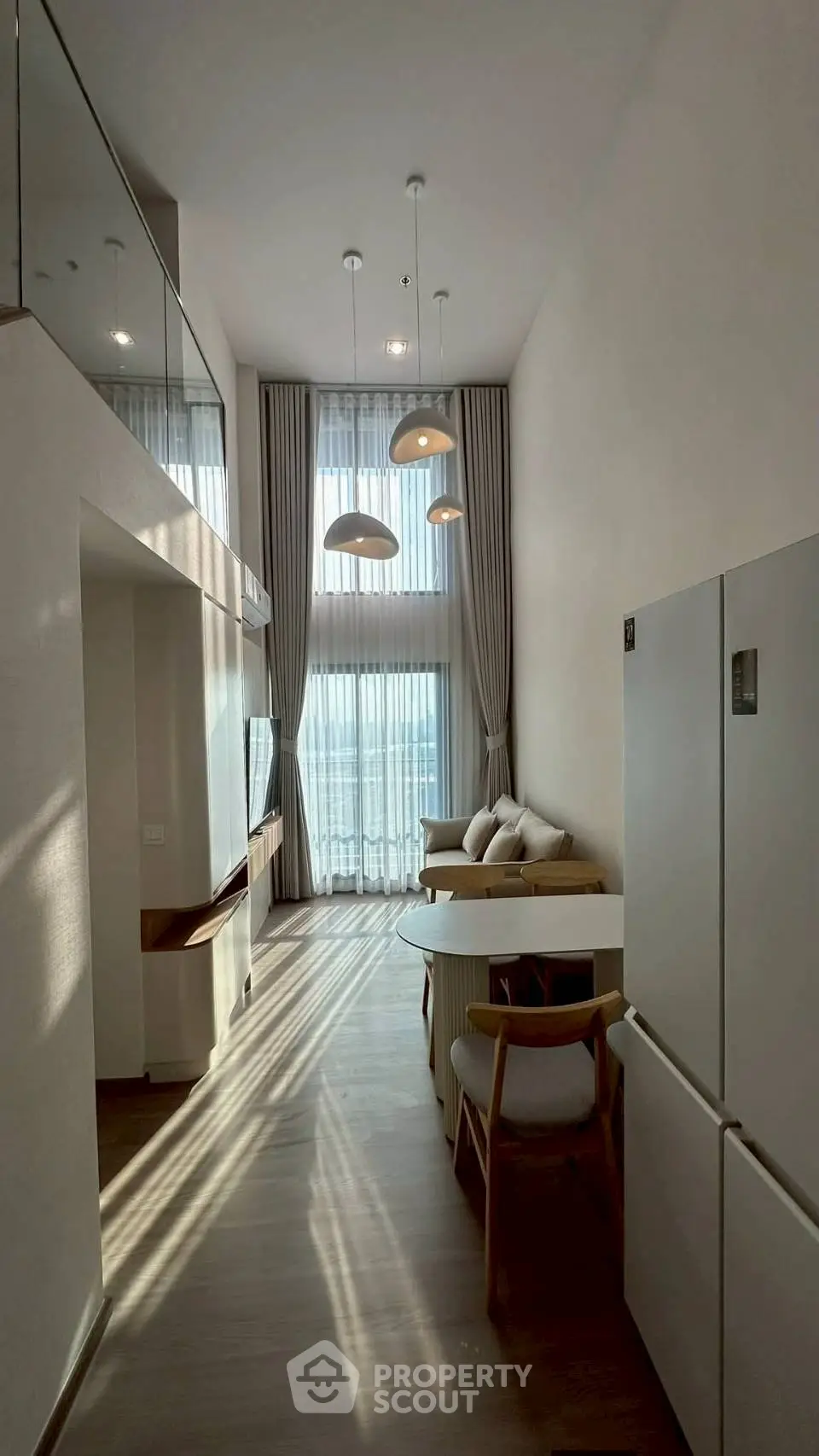 Modern living room with high ceilings and large windows, featuring stylish furniture and elegant lighting.