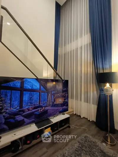 Luxurious living room with high ceilings and elegant decor, featuring a large TV and stylish curtains.