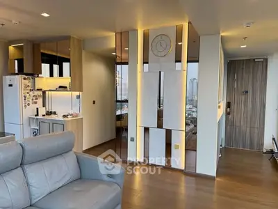 Modern living room with sleek design, featuring a leather sofa, stylish wall clock, and open kitchen layout.