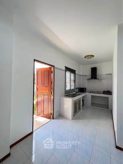 Bright kitchen with open layout and modern appliances, featuring a wooden door leading to outdoor space.