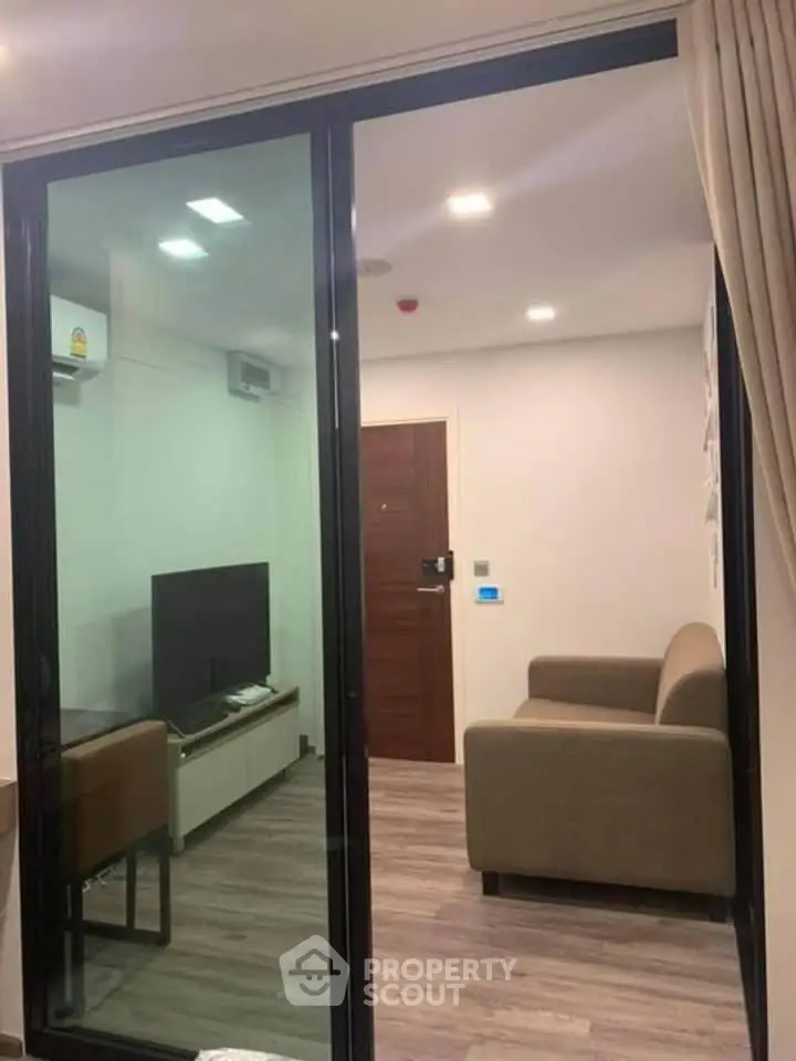 Modern living room with glass sliding door, cozy sofa, and sleek TV setup in a stylish apartment.