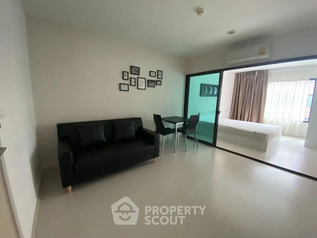 Modern living room with black sofa and dining set, adjacent to a bright bedroom.