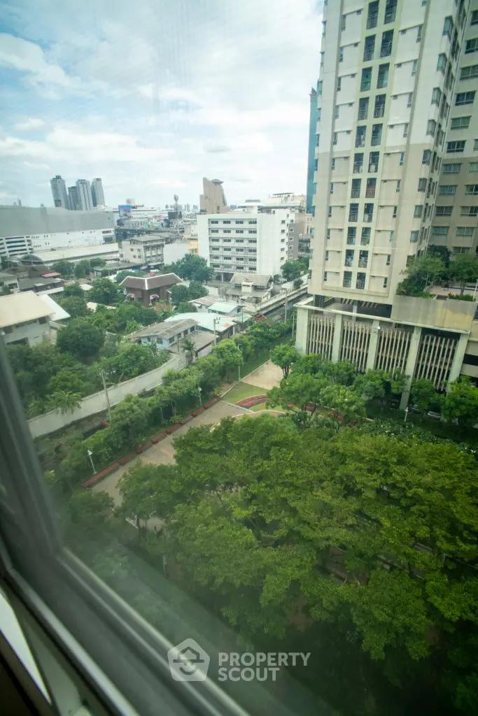 Stunning cityscape view from high-rise apartment window overlooking lush greenery and urban skyline.